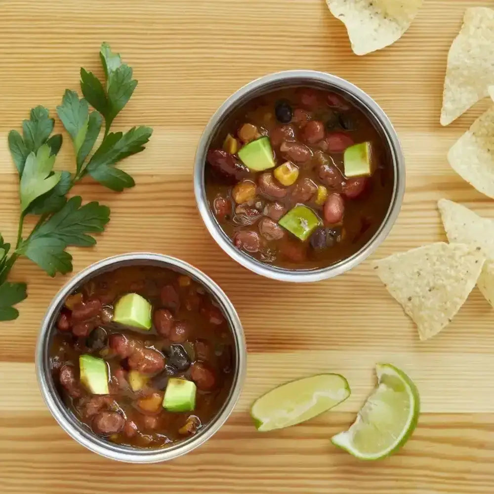 Two bowls of bean salad with tortilla chips and limes on a wooden surface