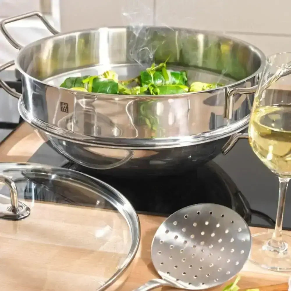 Stainless steel colander with green vegetables, a glass of white wine, and a ladle on a kitchen counter.