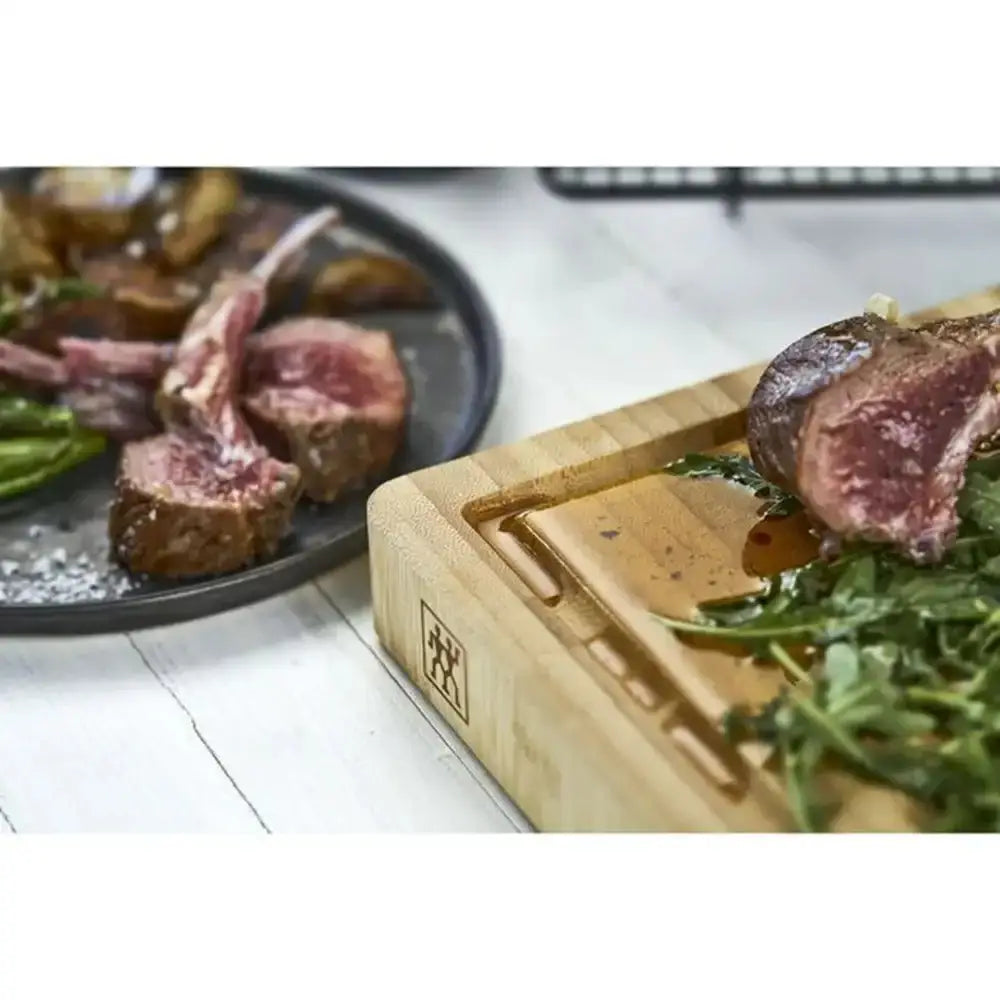 Wooden cutting board with cooked lamb chops and arugula on a white surface