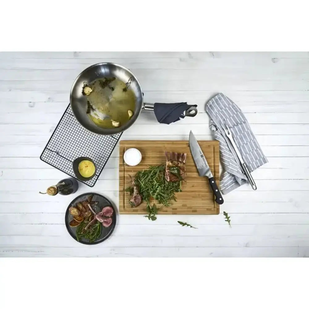Cooking scene with a frying pan, cutting board, knife, and ingredients on a white wooden surface.