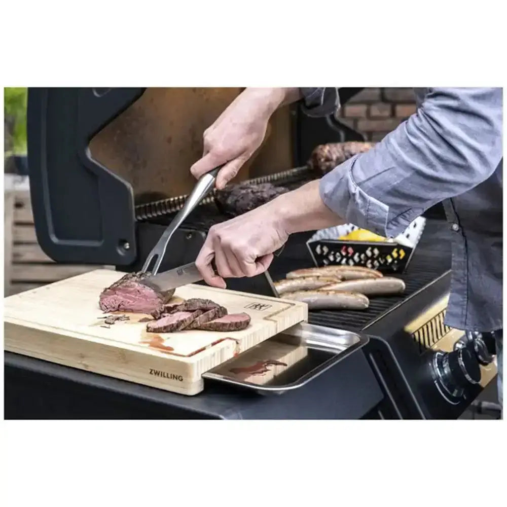 Person grilling and cutting meat on a barbecue with a cutting board and knife.
