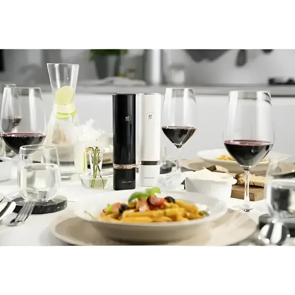 Dinner table with pasta dish, wine glasses, and a bottle of red wine.
