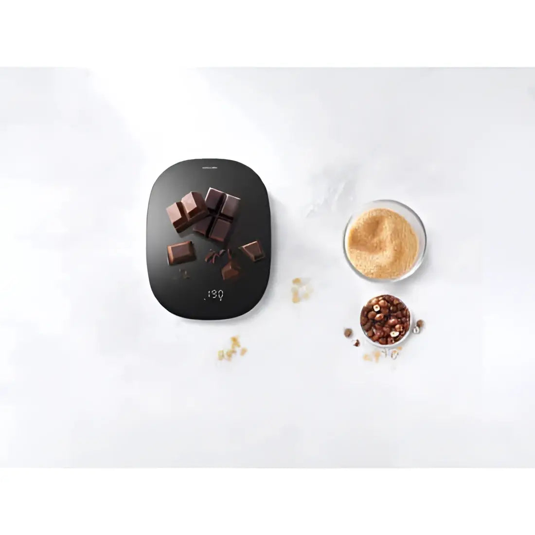 Smart kitchen scale with chocolate pieces and a bowl of spices on a white surface