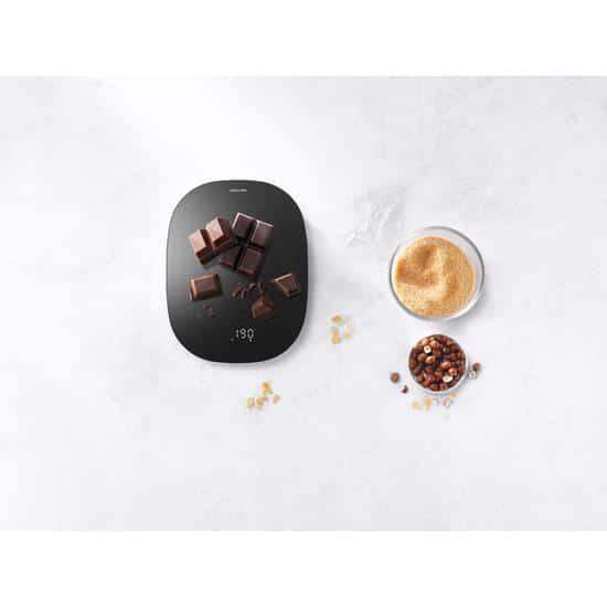 Smart kitchen scale with chocolate pieces and a bowl of spices on a white surface