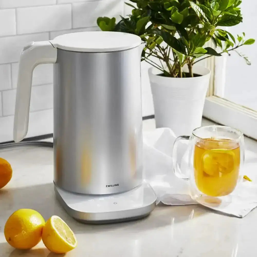 Silver electric kettle on a kitchen counter with a cup of tea and lemons.