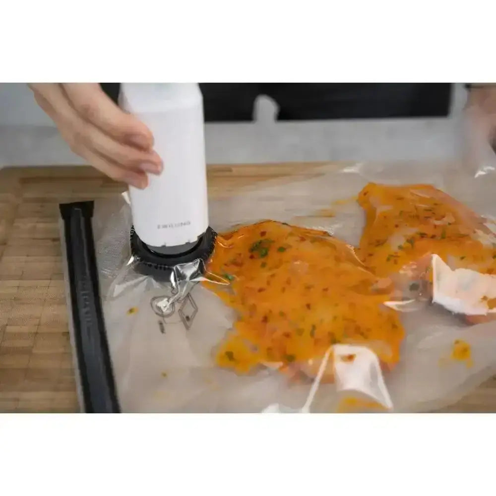 Person using a vacuum sealer to seal orange food in a clear bag on a wooden surface.
