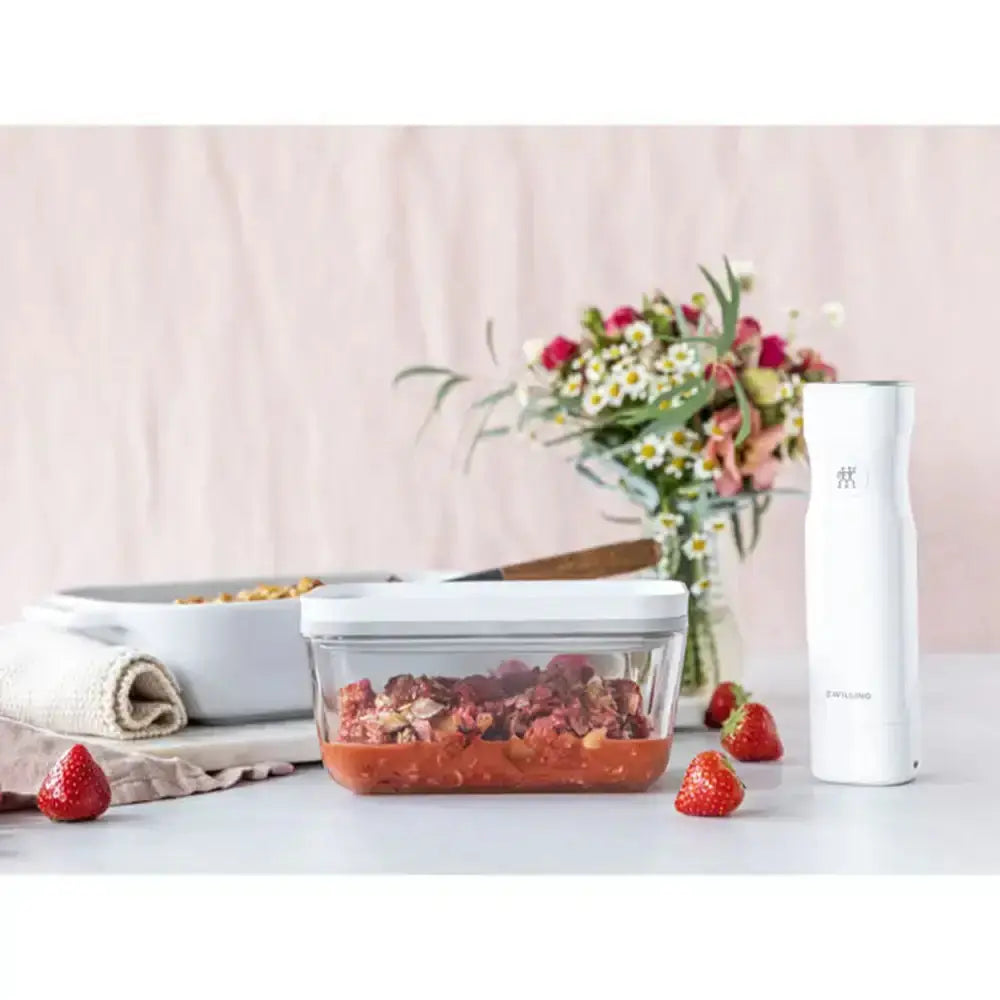 Glass food container with strawberries on a table with a pink background