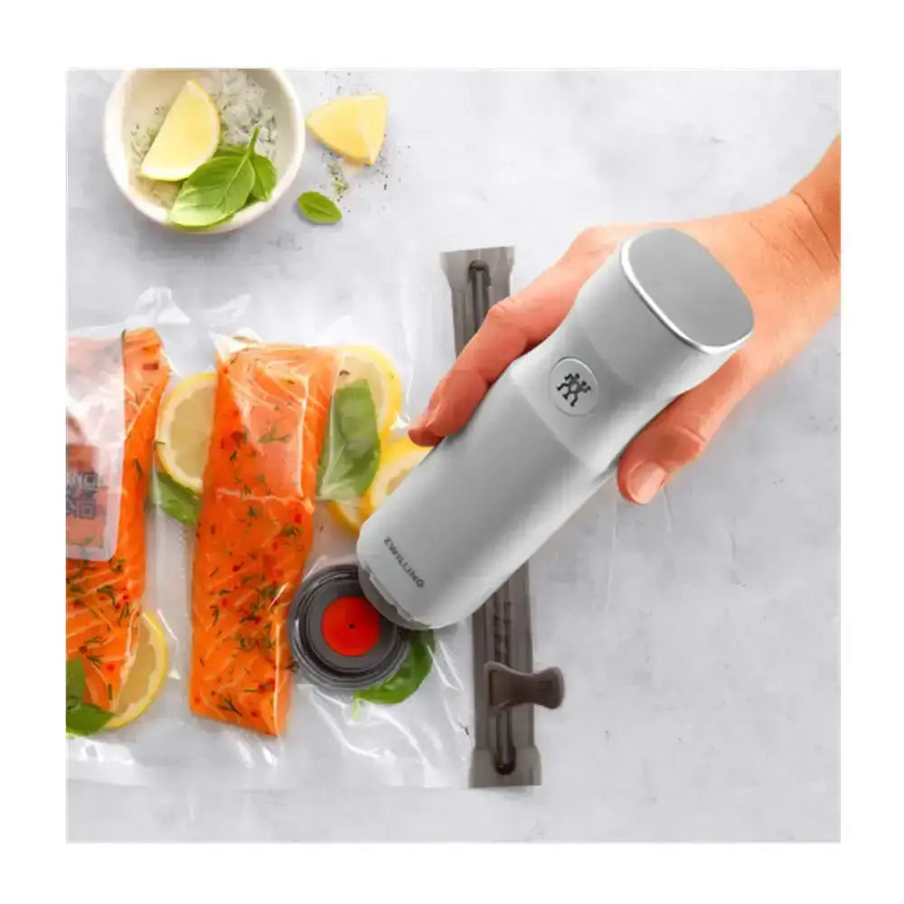 Hand using a vacuum sealer with salmon and vegetables on a table