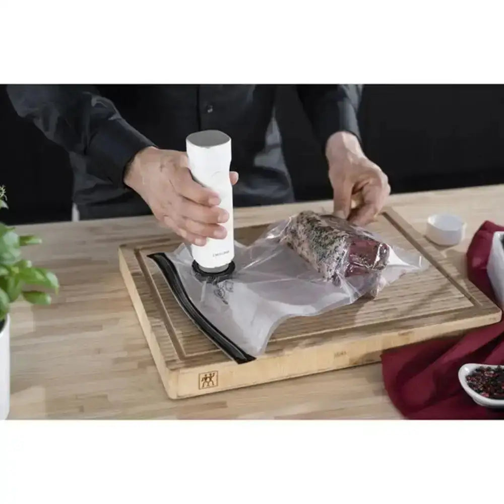 Person using a vacuum sealer on a cutting board with food packaging.