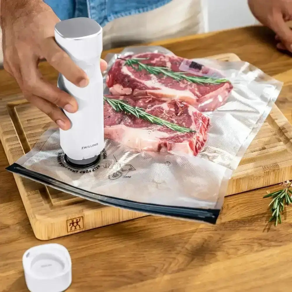 Person using a vacuum sealer on raw meat on a wooden cutting board