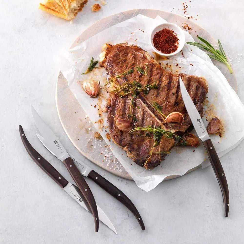 Grilled steak on a marble board with herbs and spices, accompanied by knives on a light background.
