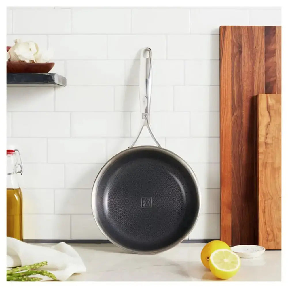 Black frying pan hanging on a wall next to a wooden cutting board with lemons and asparagus on a kitchen counter.
