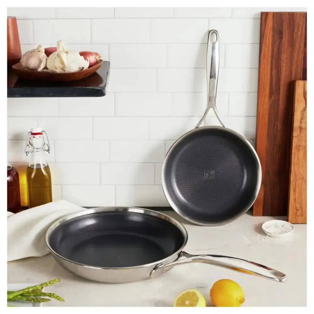 Two frying pans on a kitchen counter with lemons and garlic in the background.