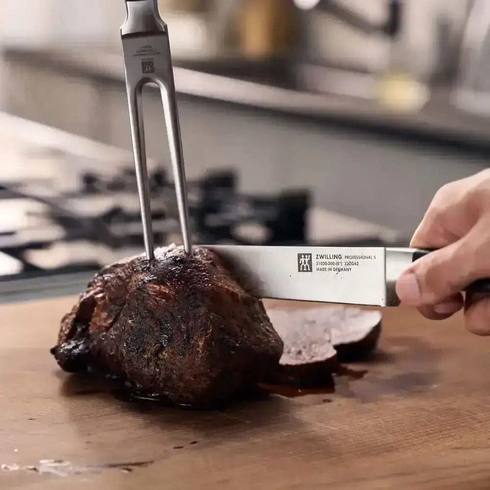 Person cutting a piece of meat with aZWILLING knife on a wooden cutting board.