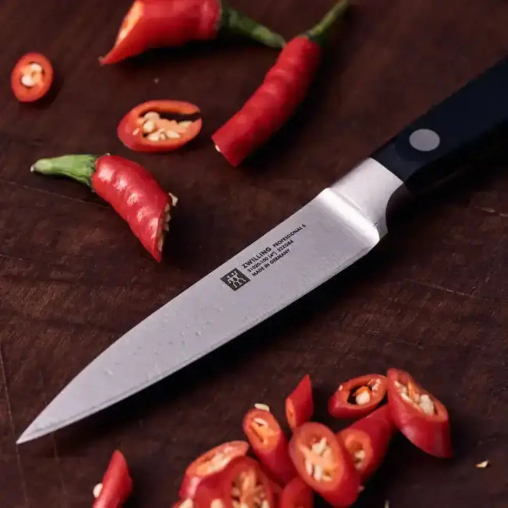 Knife with a brand logo on a wooden surface surrounded by red chili peppers