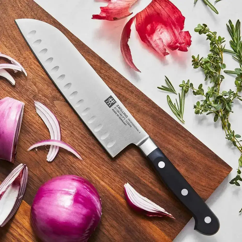 Chef's knife on a wooden cutting board with red onions and herbs