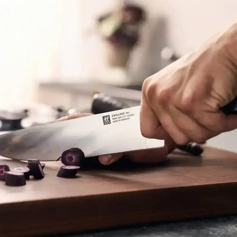 Person using a Zwilling knife to chop vegetables on a wooden cutting board.