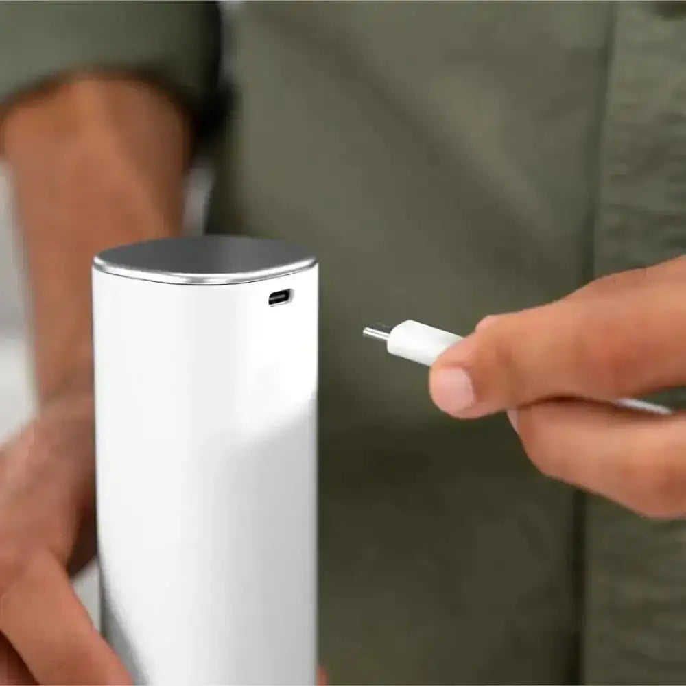 Person holding a white cylindrical device with a charging cable