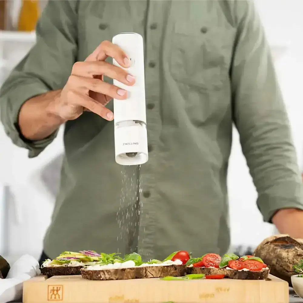 Person seasoning a dish with a white pepper grinder