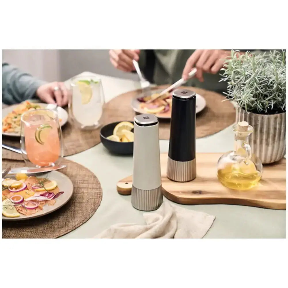 Two pepper mills on a table with food and drinks in the background