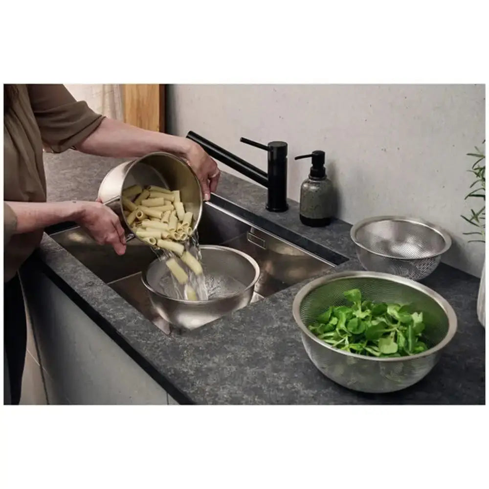 Person washing pasta in a kitchen with various bowls and a sink.