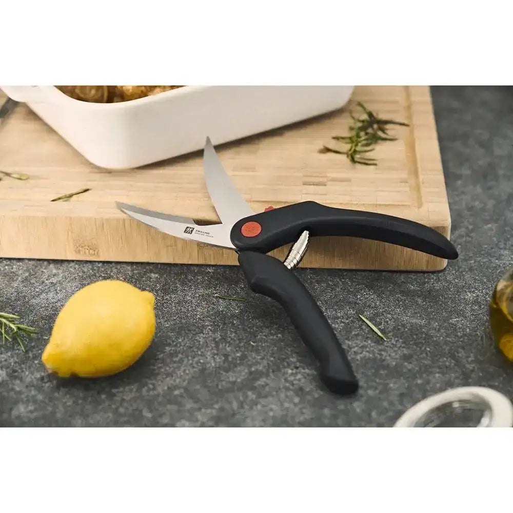 Kitchen shears on a dark surface with a lemon and cutting board in the background