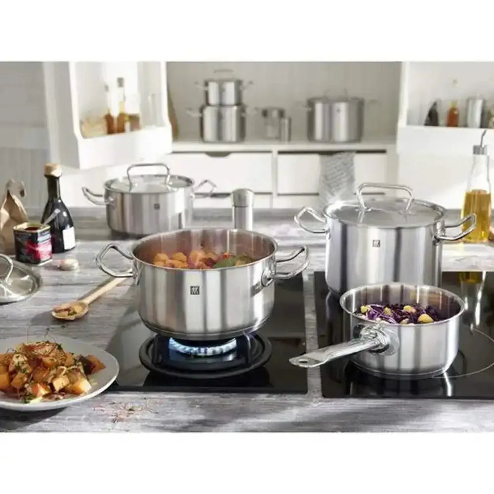 Stainless steel cookware set on a kitchen stove with food.