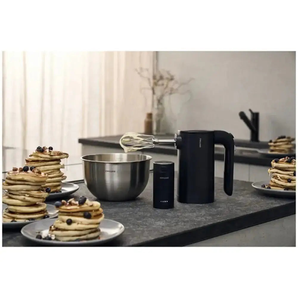 Kitchen counter with kitchen appliances and pancakes, featuring a black kettle and whisk.